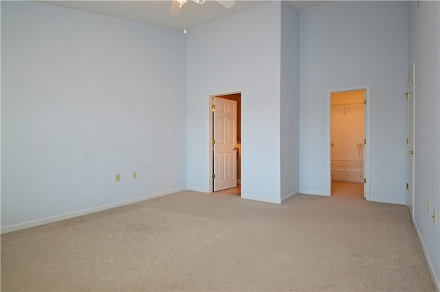 unfurnished room with light carpet, baseboards, a high ceiling, and ceiling fan