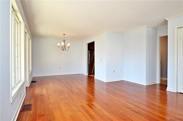 spare room featuring visible vents, a notable chandelier, wood finished floors, and ornamental molding