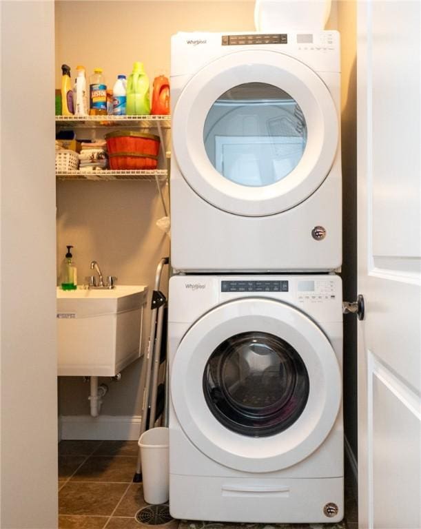 clothes washing area with a sink, stacked washer / drying machine, and tile patterned floors