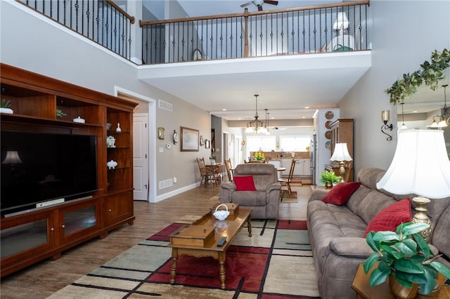 living area with visible vents, baseboards, wood finished floors, and a towering ceiling