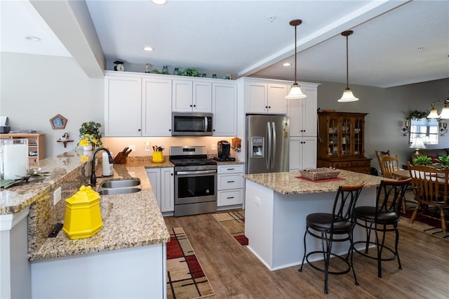 kitchen with wood finished floors, appliances with stainless steel finishes, a breakfast bar area, and a sink