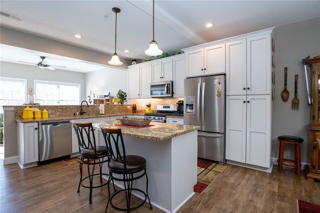 kitchen featuring visible vents, a breakfast bar, appliances with stainless steel finishes, a peninsula, and dark wood-style flooring