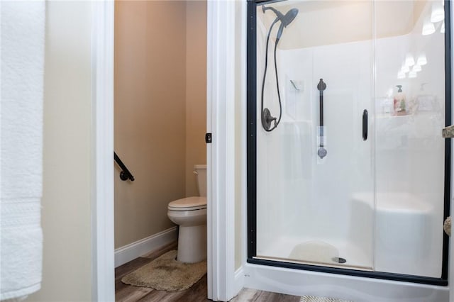 full bath with toilet, wood finished floors, a stall shower, and baseboards