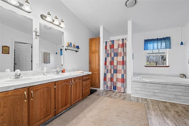 bathroom featuring a garden tub, a sink, wood finished floors, double vanity, and vaulted ceiling