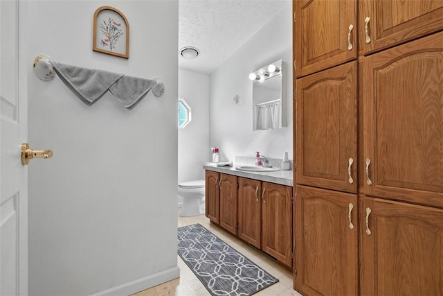 bathroom with a textured ceiling, toilet, vanity, and baseboards