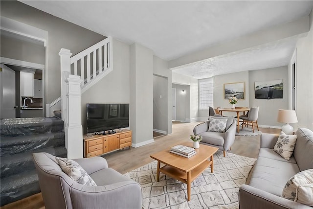 living room featuring light wood finished floors, stairway, and baseboards