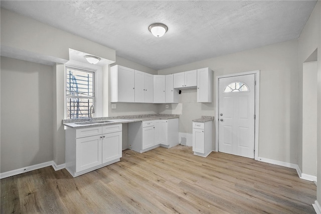 kitchen with light wood-style flooring, baseboards, white cabinets, and a sink