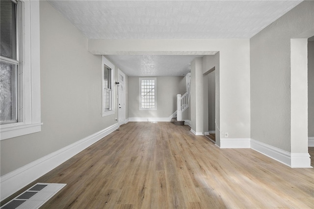 unfurnished living room with visible vents, baseboards, stairway, wood finished floors, and a textured ceiling