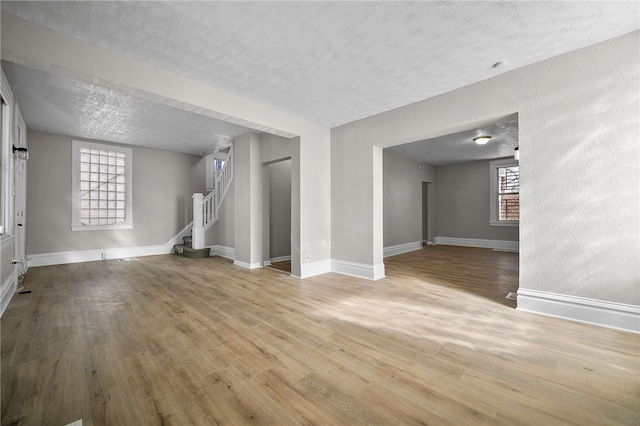 unfurnished living room with stairway, plenty of natural light, a textured ceiling, and wood finished floors