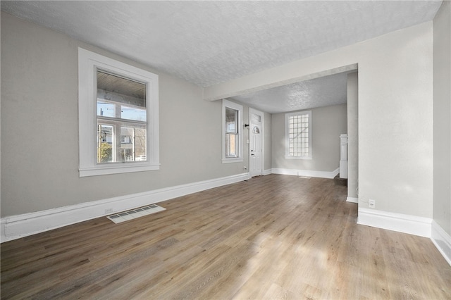 unfurnished living room with baseboards, wood finished floors, visible vents, and a textured ceiling