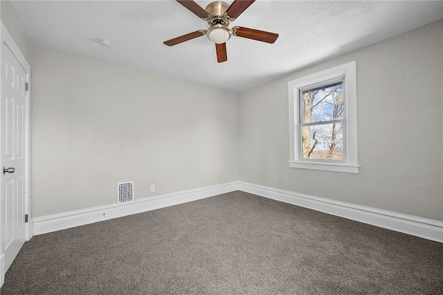 empty room featuring visible vents, dark carpet, baseboards, and a ceiling fan