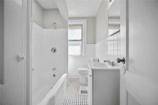 bathroom featuring vanity, a wainscoted wall, tub / shower combination, tile walls, and toilet