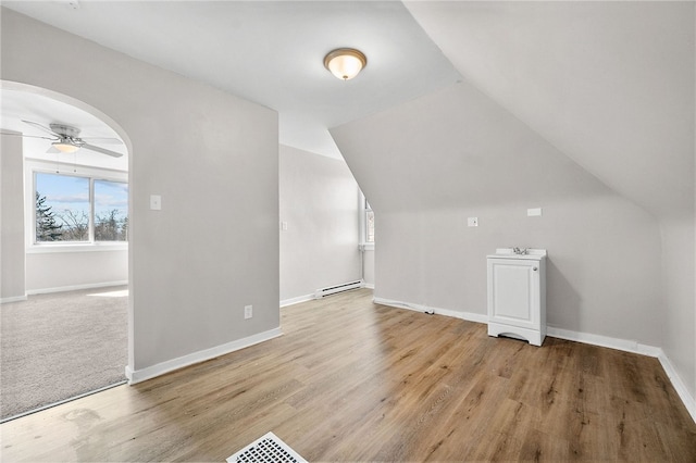 additional living space featuring arched walkways, a baseboard heating unit, ceiling fan, and wood finished floors