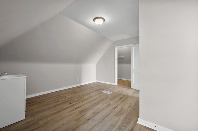 additional living space with visible vents, a sink, wood finished floors, baseboards, and vaulted ceiling