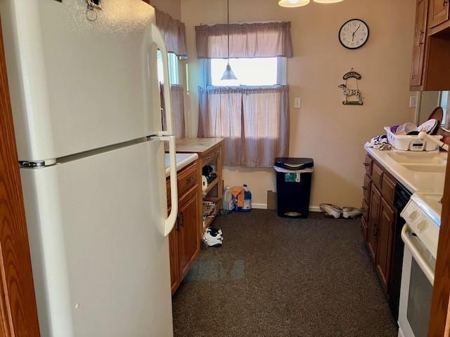 kitchen featuring light countertops, carpet flooring, brown cabinets, freestanding refrigerator, and a sink