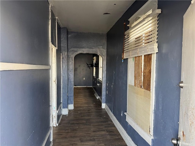 hallway featuring baseboards, arched walkways, and wood finished floors