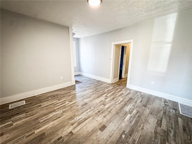 spare room featuring visible vents, a textured ceiling, baseboards, and wood finished floors