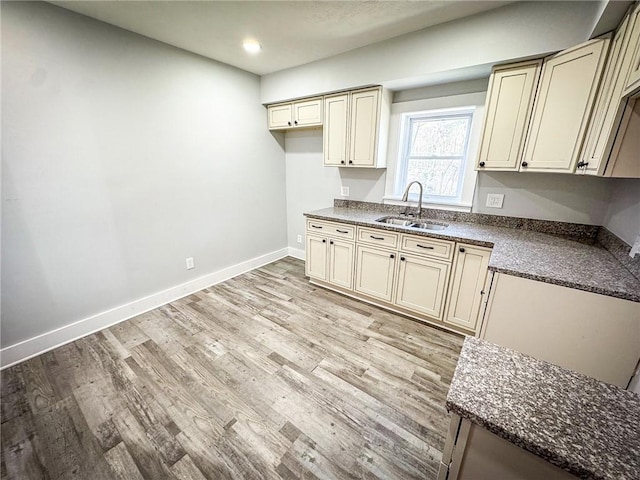 kitchen with a sink, baseboards, cream cabinetry, and light wood-style flooring