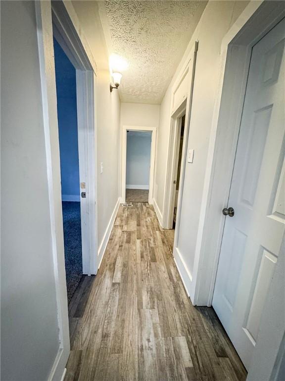 hall featuring a textured ceiling, baseboards, and wood finished floors