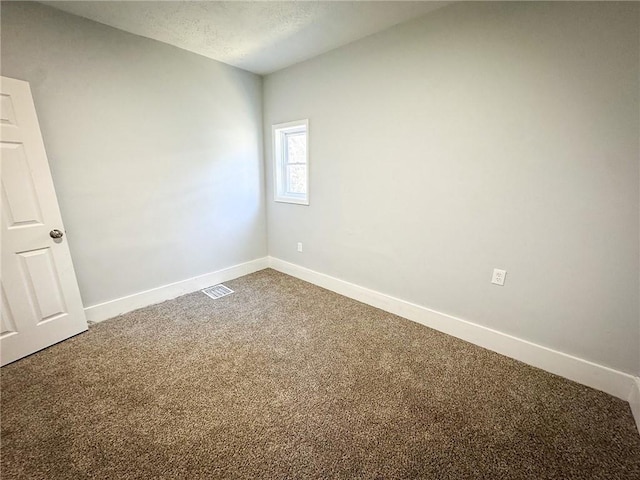 empty room featuring dark colored carpet, visible vents, baseboards, and a textured ceiling