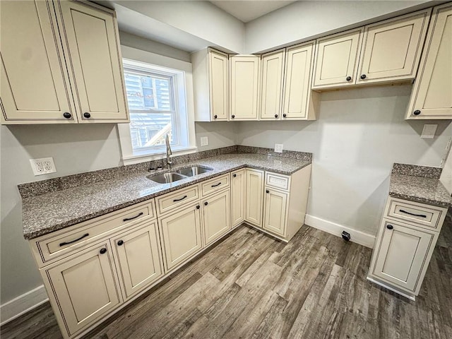 kitchen featuring stone counters, cream cabinets, dark wood-type flooring, and a sink