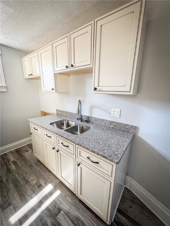 kitchen featuring light stone countertops, baseboards, dark wood finished floors, a sink, and a textured ceiling