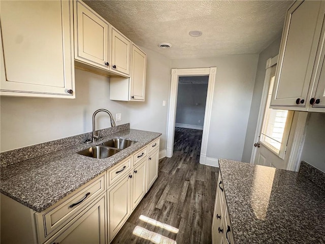 kitchen featuring visible vents, dark wood-type flooring, baseboards, dark stone countertops, and a sink