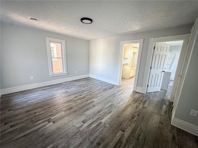 unfurnished bedroom with visible vents, connected bathroom, baseboards, dark wood finished floors, and a textured ceiling