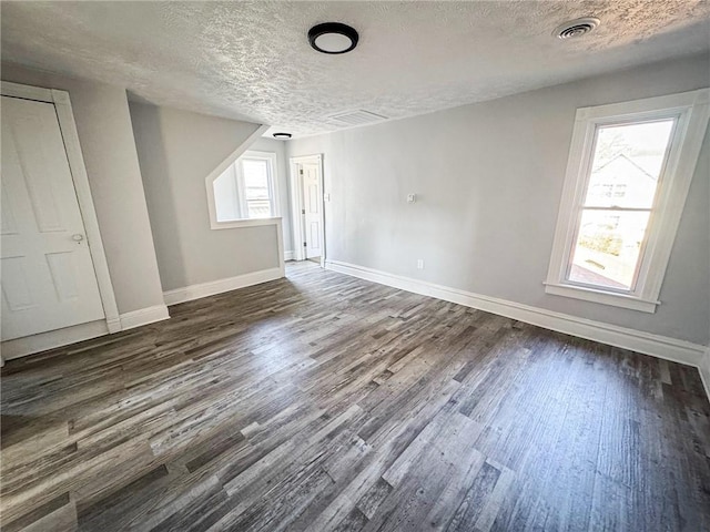 interior space with dark wood finished floors, visible vents, a textured ceiling, and baseboards