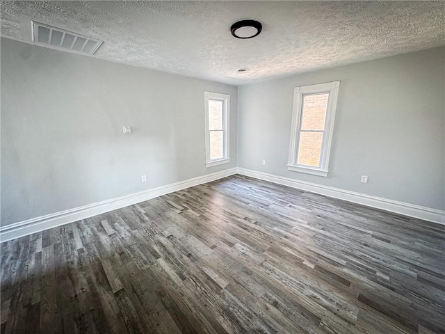 empty room with dark wood finished floors, baseboards, visible vents, and a textured ceiling