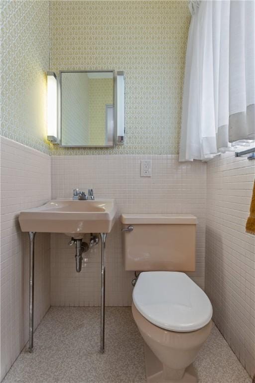 half bath with a wainscoted wall, toilet, wallpapered walls, and tile walls