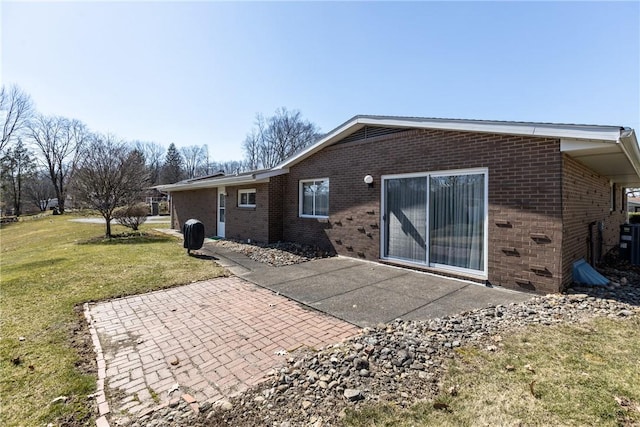 rear view of property featuring a patio, a lawn, and brick siding