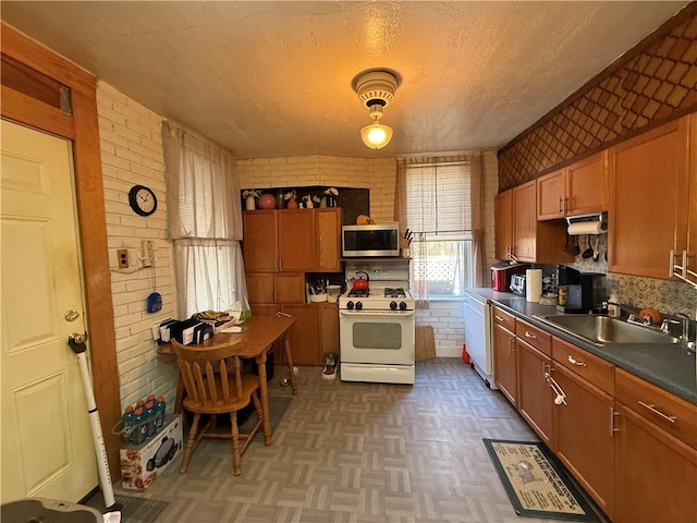 kitchen with a sink, stainless steel microwave, dark countertops, brick wall, and white gas range