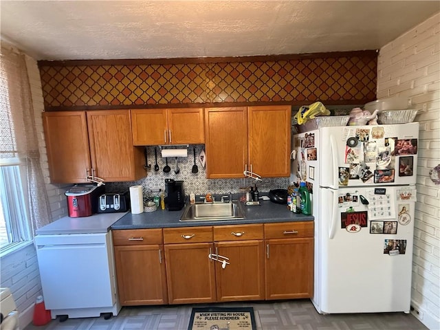 kitchen with dark countertops, brown cabinetry, freestanding refrigerator, and a sink