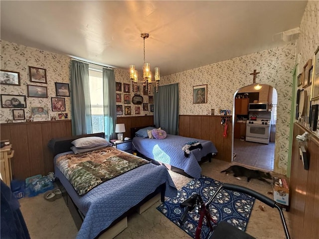 carpeted bedroom with arched walkways, an inviting chandelier, wainscoting, and wallpapered walls