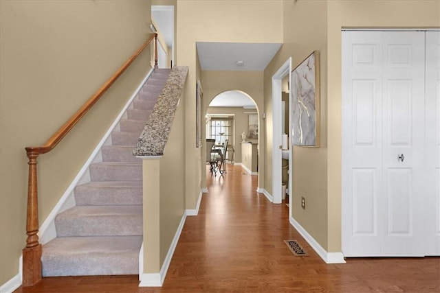 foyer entrance featuring arched walkways, stairway, baseboards, and wood finished floors