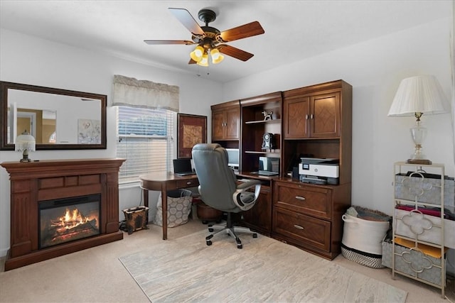 office area featuring light colored carpet, a glass covered fireplace, and a ceiling fan