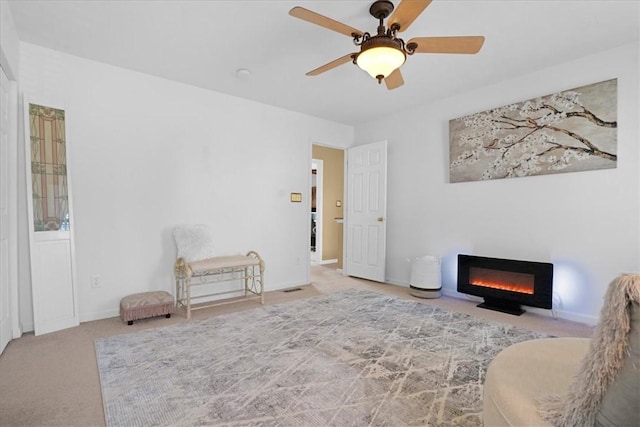 living area featuring baseboards, carpet floors, a glass covered fireplace, and a ceiling fan