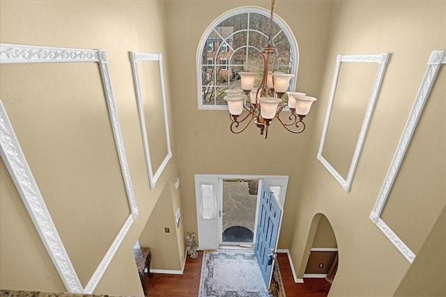 entryway with a towering ceiling, baseboards, an inviting chandelier, and wood finished floors