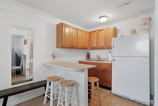 kitchen with visible vents, light countertops, a kitchen breakfast bar, freestanding refrigerator, and a sink