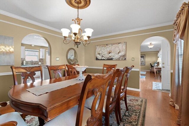 dining room with wood finished floors, baseboards, arched walkways, ornamental molding, and a notable chandelier