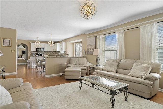 living room featuring arched walkways, a chandelier, baseboards, and wood finished floors