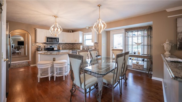 dining room featuring baseboards, arched walkways, an inviting chandelier, and dark wood finished floors