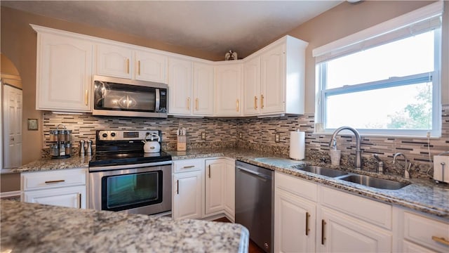 kitchen with a sink, light stone countertops, appliances with stainless steel finishes, and white cabinetry