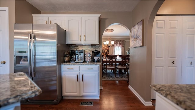 kitchen featuring stainless steel refrigerator with ice dispenser, light stone counters, arched walkways, white cabinets, and a chandelier