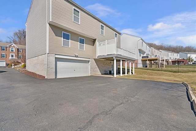 rear view of property with driveway, a residential view, brick siding, fence, and an attached garage