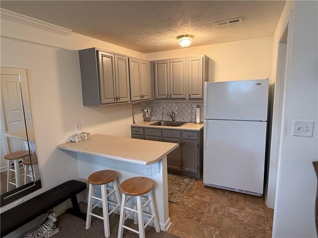 kitchen featuring gray cabinets, visible vents, a sink, freestanding refrigerator, and a breakfast bar