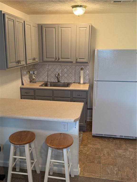 kitchen featuring freestanding refrigerator, a kitchen breakfast bar, gray cabinetry, and a sink