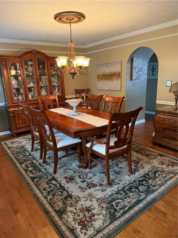 dining space with arched walkways, wood finished floors, baseboards, a chandelier, and ornamental molding