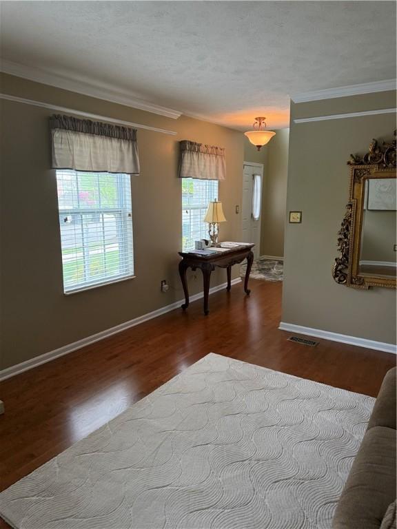 living area featuring baseboards, visible vents, ornamental molding, and wood finished floors